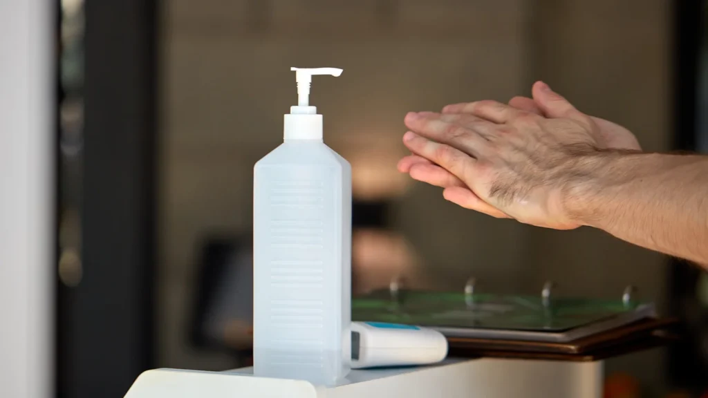 Flacone dispenser con pompa per igienizzante mani e persona che si disinfetta le mani sullo sfondo.