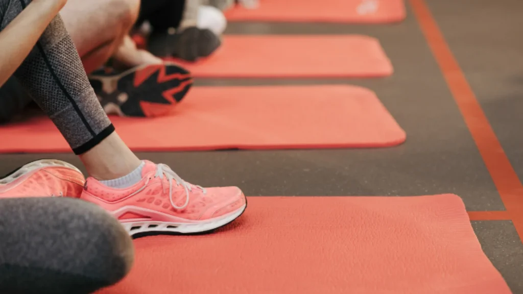 Piede con scarpa da ginnastica rosa su tappetino yoga rosso in una palestra.