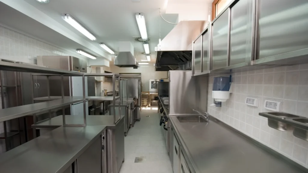 Cucina professionale da ristorante in acciaio inox pulita e sanificata con piani di lavoro e cappe industriali.