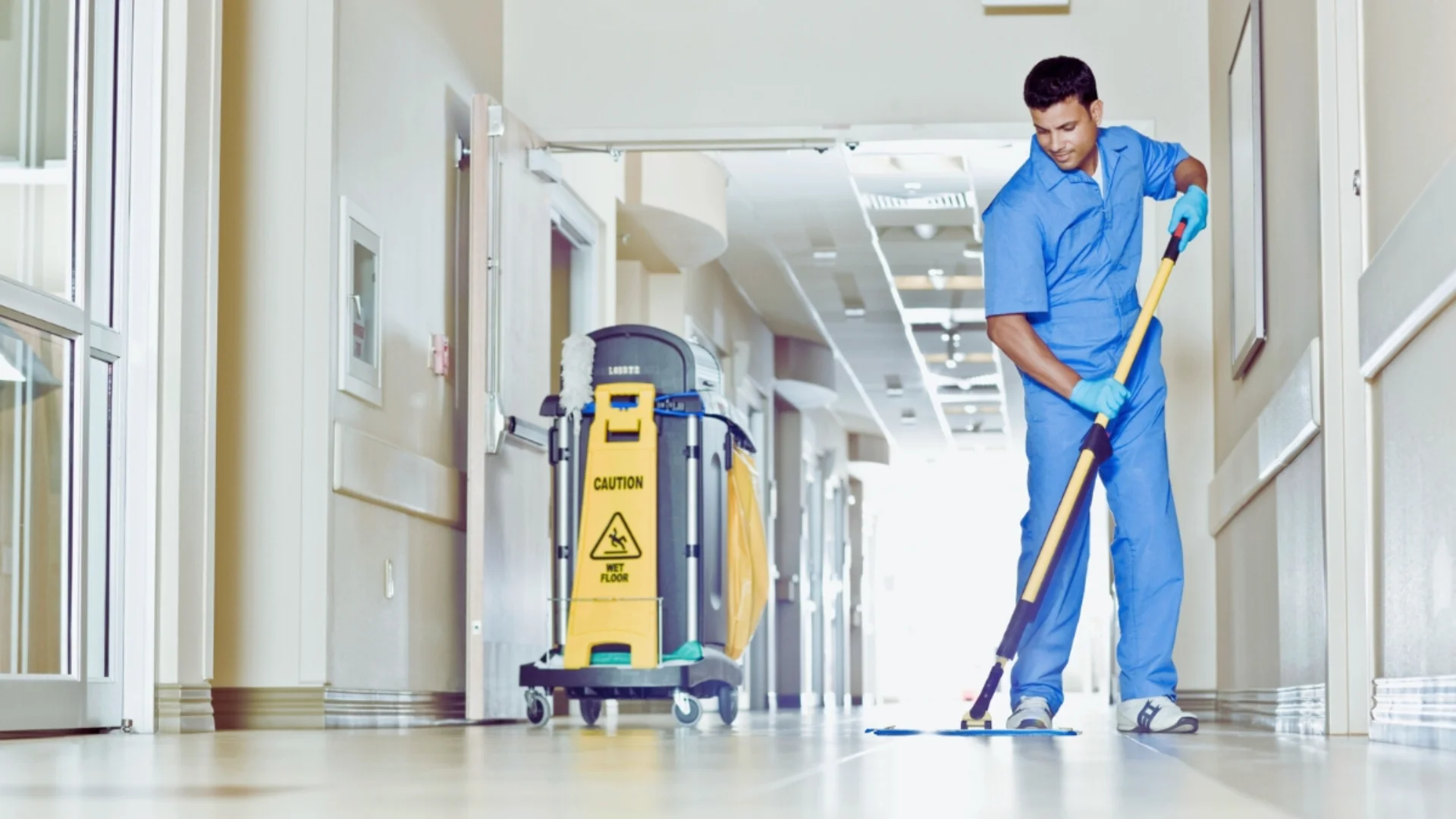Operatore con divisa medica azzurra esegue la sanificazione dei pavimenti lucidi di un ambiente sterile.