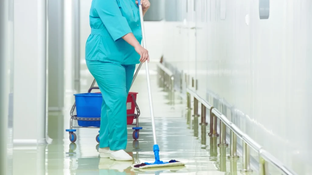 Operatore in divisa azzurra lava il pavimento del corridoio di un ospedale con mop professionale.